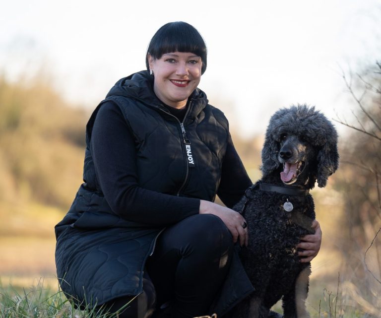 Trainerin sitzt in Hocke mit ihrem Hund im Arm