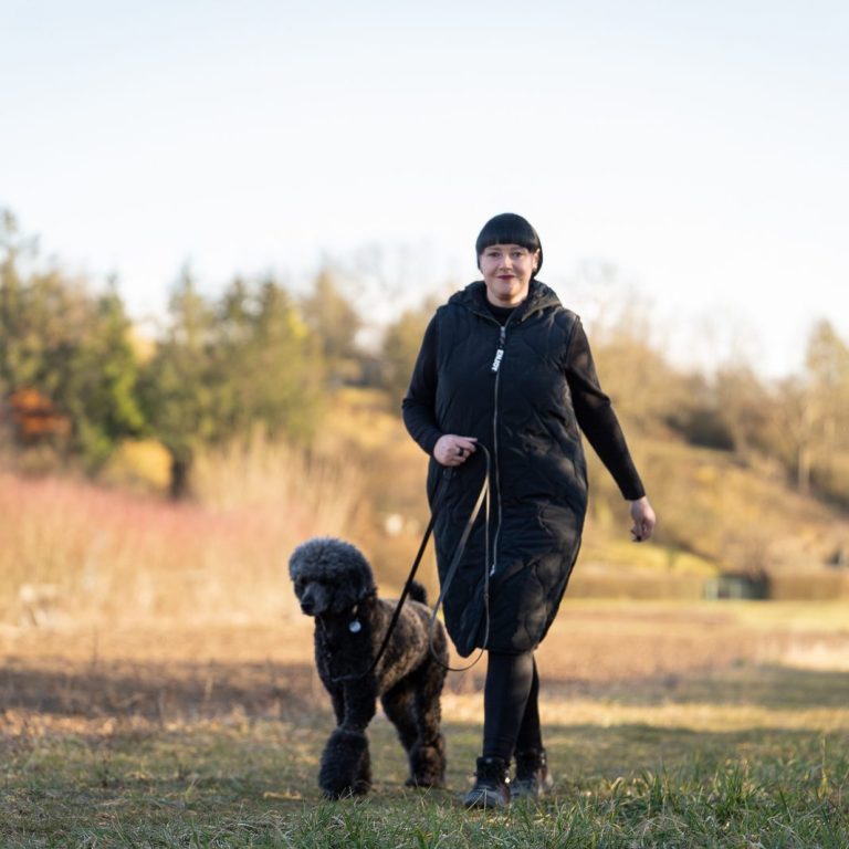 Trainerin läuft mit Ihrem Hund Bei Fuß an der Leine auf einer Wiese